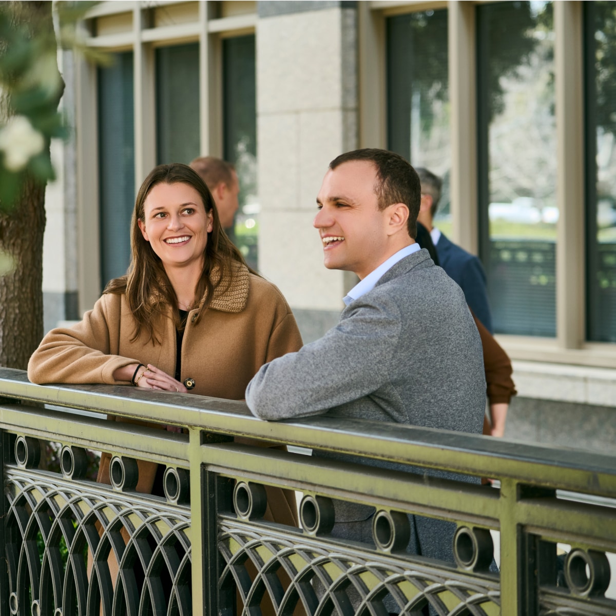 2 people standing next to a railing and smiling while looking into the distance